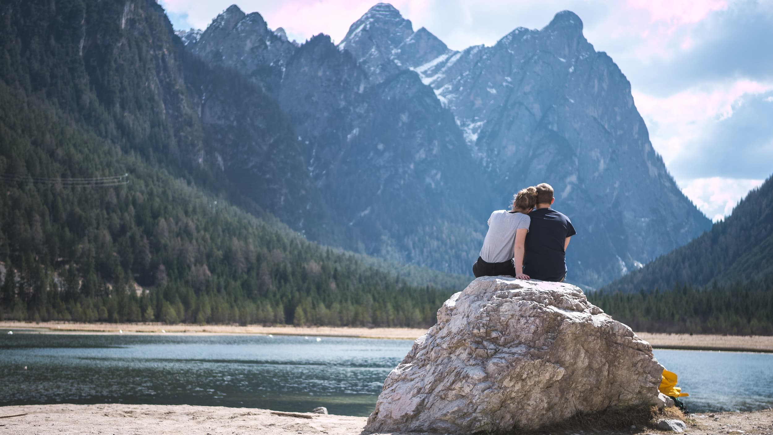 couple sitting on a rock in front of an alpine lake