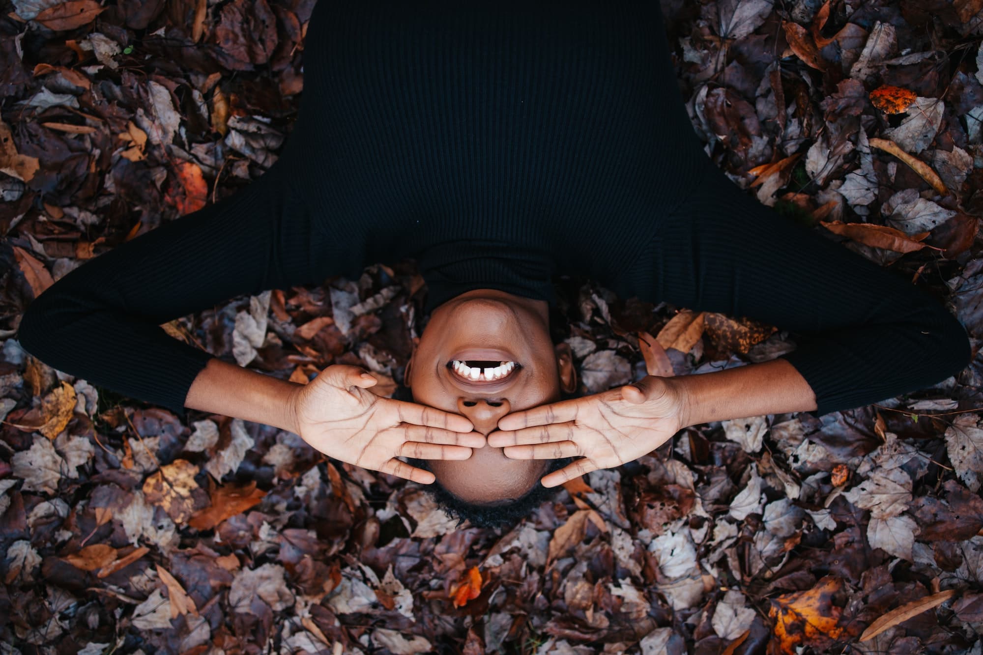 Person laying in pile of fall leaves and laughing