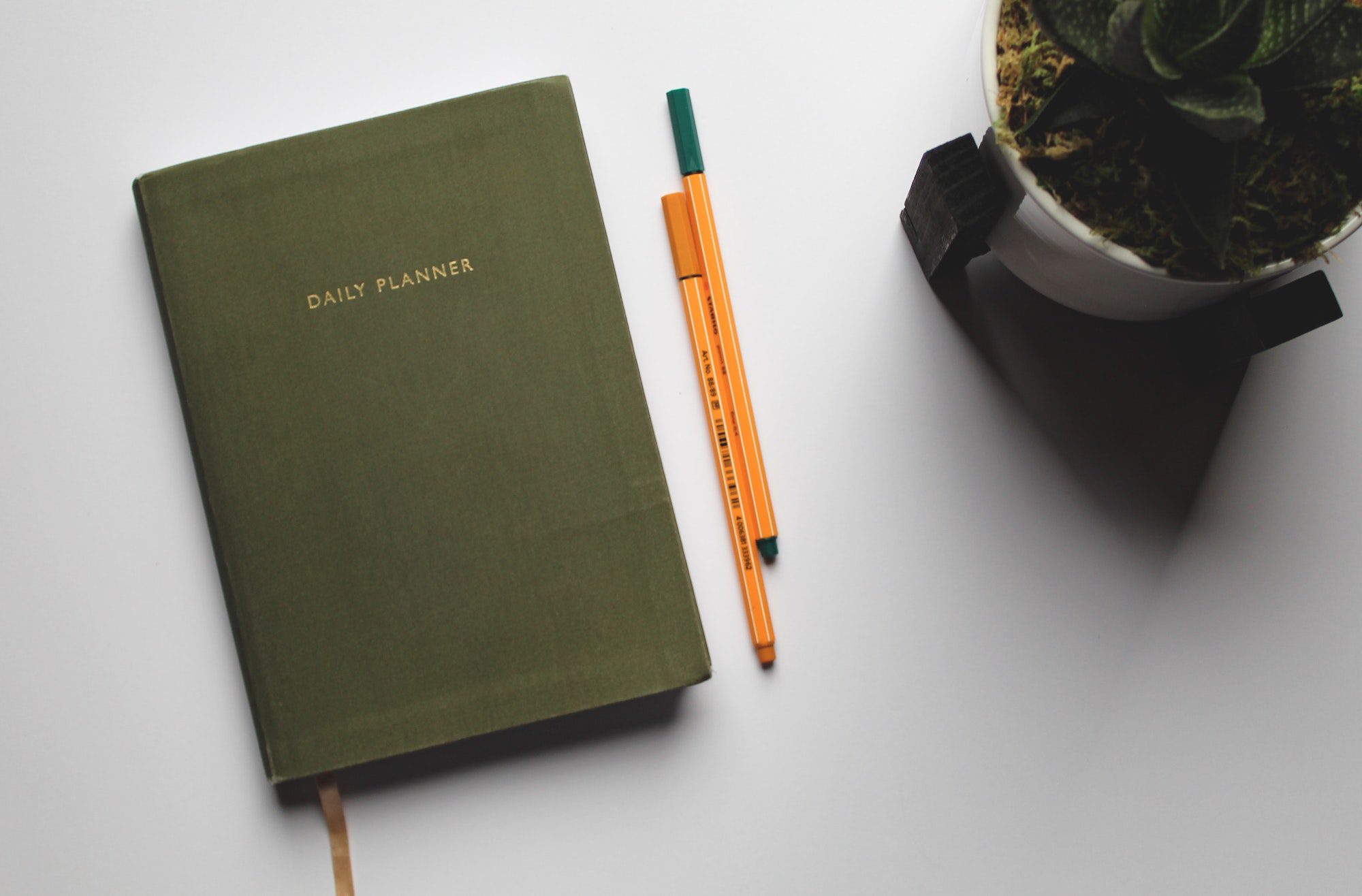 Daily planner on a table with a potted plant and pens