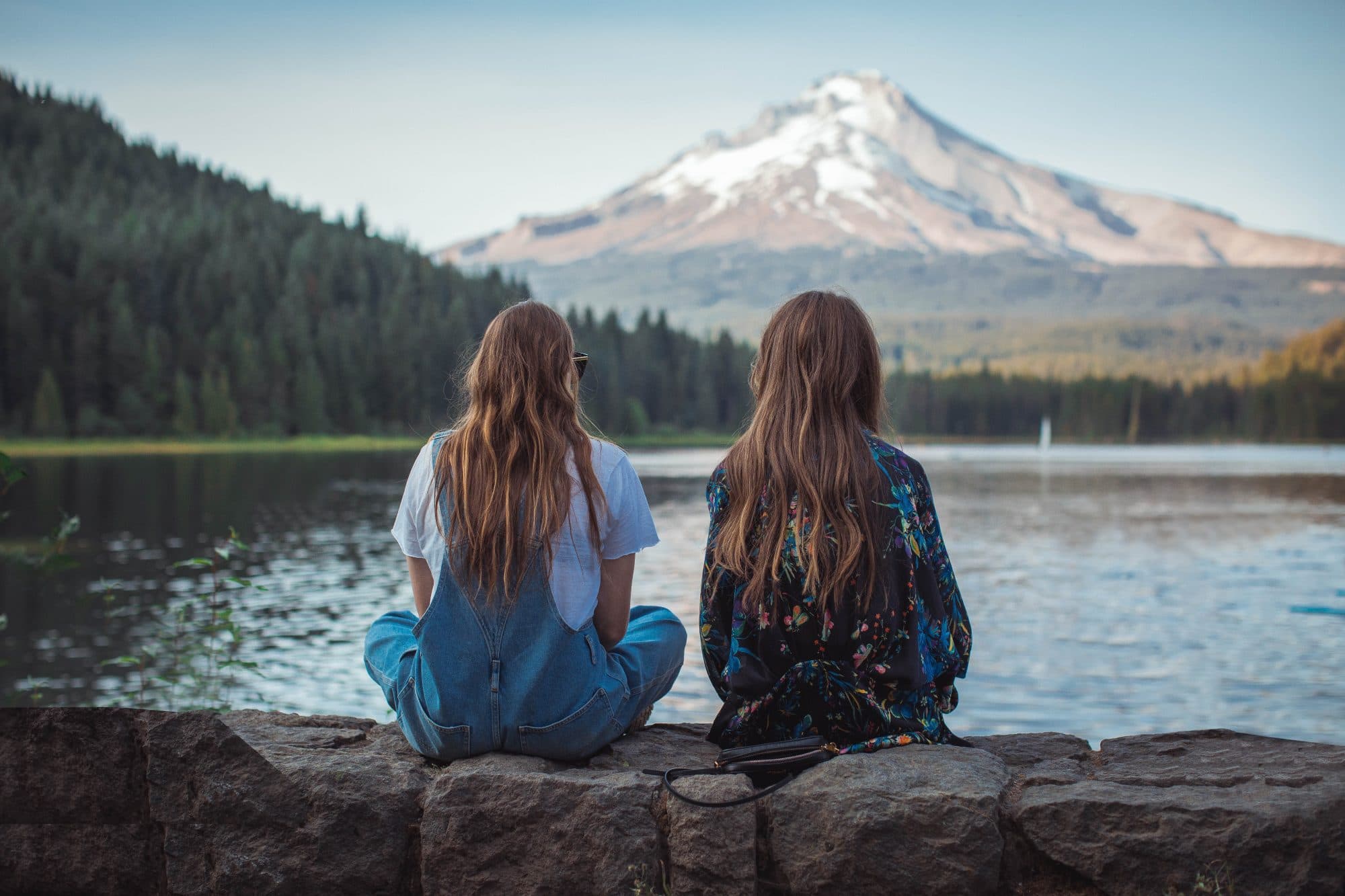 Two sisters sitting on front of a lake in the mountains