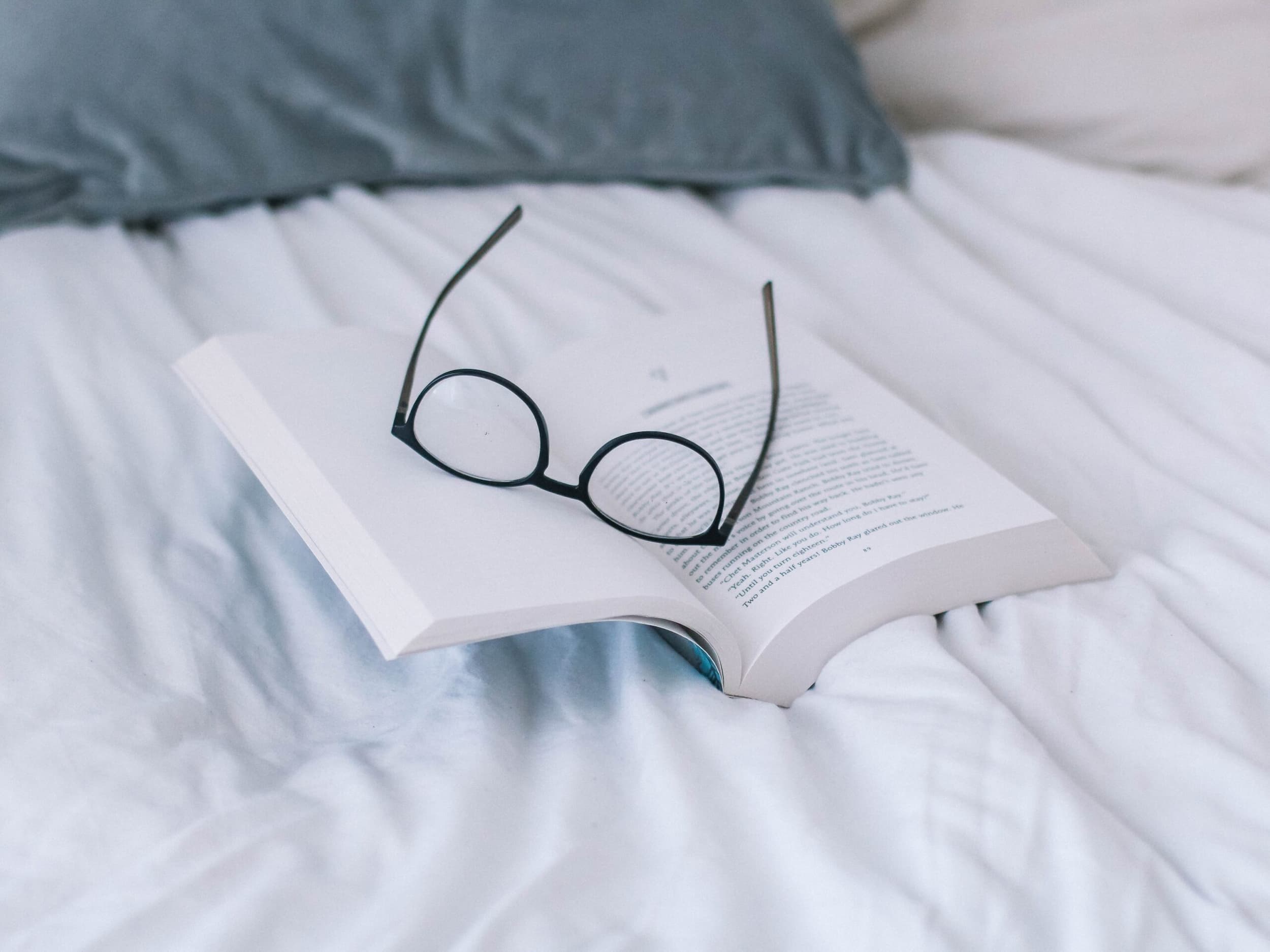 Photo of an open book with glasses on top on a bed