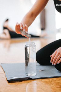 Pouring a packet of LMNT into a water bottle next to a yoga mat