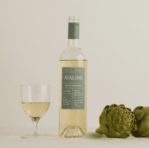 A bottle and glass of white wine next to a couple of artichokes