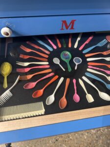 A drawer of colorful plastic spoons, forks, combs, and other items arranged in precise geometric arrays.