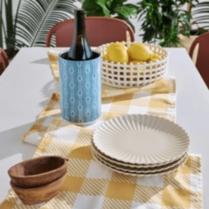 Dishes and linens in white, blue, and yellow arranged on an outdoor table with plants int he background