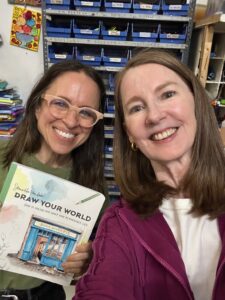 Selfie of Gretchen and a friend posing with a watercolor book titled "Draw Your World"