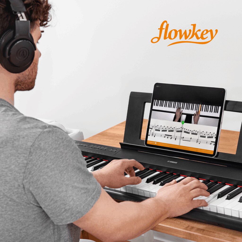 A tablet shows the flowkey app while a user plays a piano