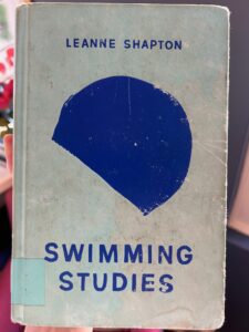 Photo of the book Swimming Studies by Leanne Shapton. The cover art features an illustration of a blue semi-circle which, upon closer examination, resembles a swimming cap