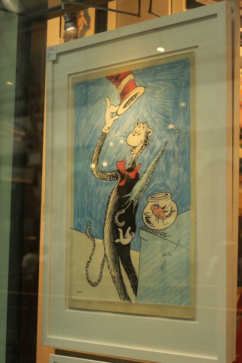The cat in the hat balancing a red striped hat.