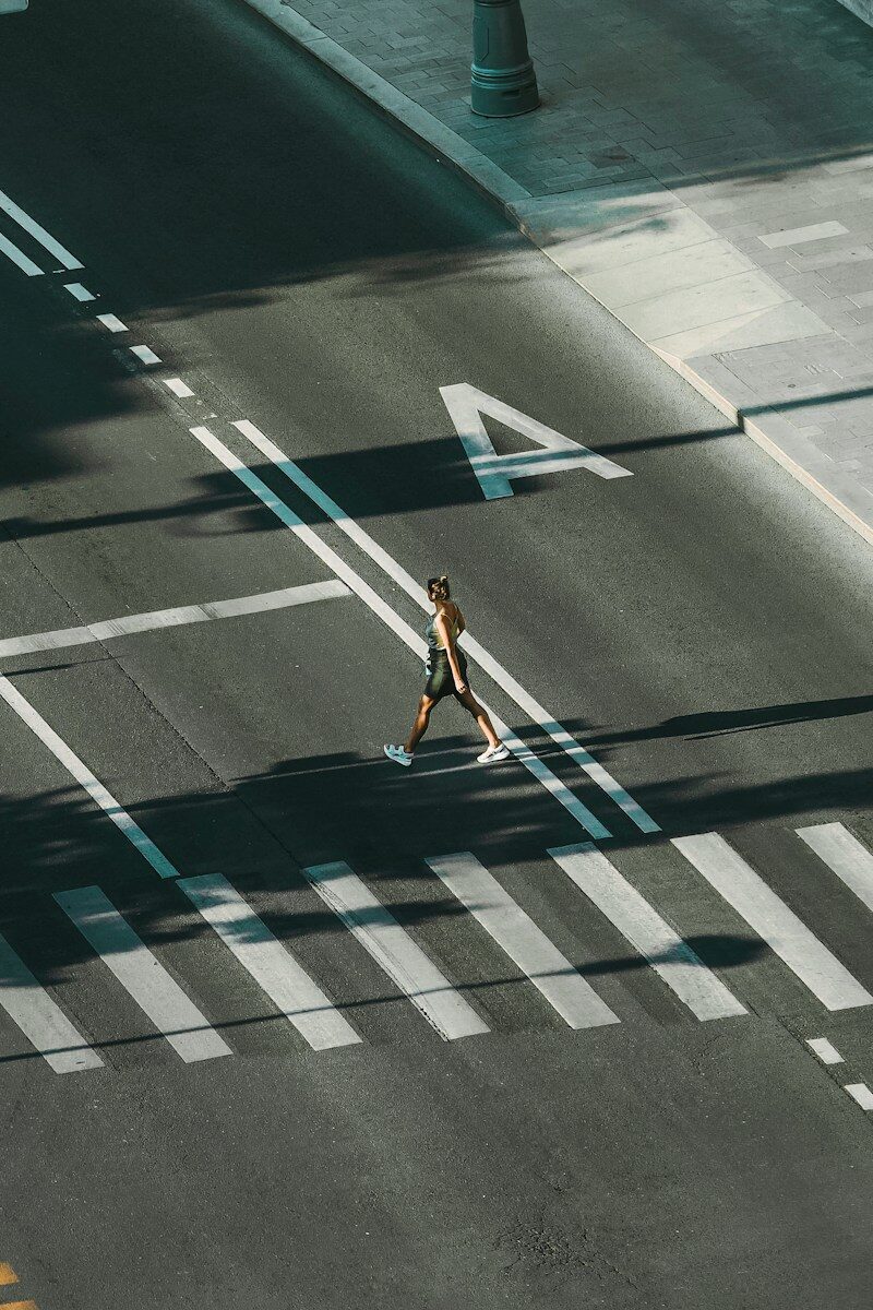 woman in white tank top and blue denim shorts walking on pedestrian lane during daytime