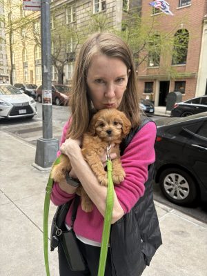 Gretchen and Taffy Gretchen on a city sidewalk holding Taffy, a small brown puppy with curly fur.